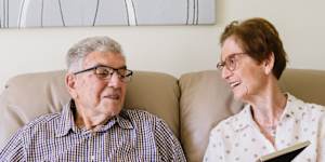 Peter and Stella Samios at home in Brisbane,October 2025. They are looking at their wedding portrait from 1963.