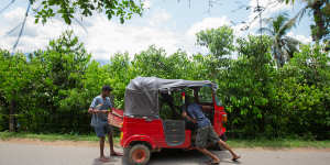 Young men push a stalled tuk-tuk on a road through a cinnamon plantation in Kuruwita. 
