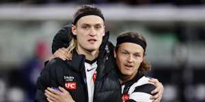 Captain Darcy Moore,jacket on,puts his arm around substitute Jack Ginnivan.