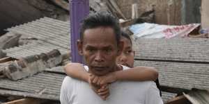 A man carries his son past ruins of houses damaged in Monday’s earthquake in Cianjur.