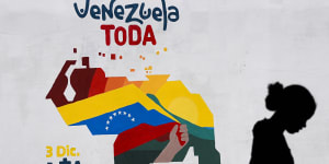 A woman sells fruit in front of a mural of a Venezuelan map with the Essequibo territory (bottom right of map) included and the words “All of Venezuela. Vote yes five time on December 3”,in Caracas.