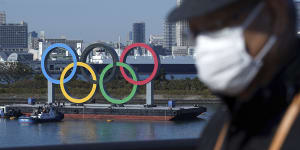 A man wearing a protective face mask to help curb the spread of the coronavirus walks with the Olympic rings in the background in Odaiba. 