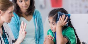 Young female soccer athlete is dazed while ER doctor asks her questions. The girl has an icepack on her head. The girl’s mom is in the background. Credit:iStock GENERIC INJURED CHILD