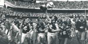 Peter Bosustow,premiership cup in hand and Carlton scarf flowing,leads the triumphant Blues on a victory lap of the MCG after the 1982 grand final.