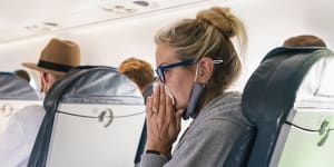 Woman sitting on a plane blowing her nose. 