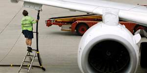A ground staff member stands beside a fuel attachment to a Qantas plane at Sydney Airport.