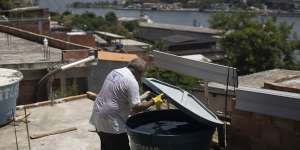 Augusto Cesar,a city worker who combats endemic diseases,inspects a water tank where mosquitoes can breed in the Morro da Penha favela in Niteroi,Brazil,the Rio-Niteroi Bridge in the background.
