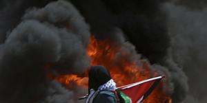 A Palestinian woman walks past burning tires near the Israeli border.