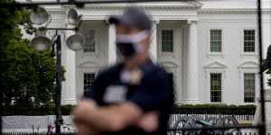 A uniformed Secret Service agent stands on the street in front of the White House.