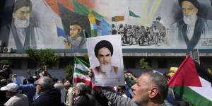 People walk past a mural showing Ayatollah Khomeini,right,Supreme Leader Ayatollah Ali Khamenei,left,while holding a poster of Ayatollah Khomeini and Iranian and Palestinian flags in an anti-Israeli march after Friday prayers in Tehran.