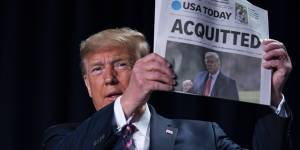 Donald Trump holds up a newspaper following his acquittal in the Senate.