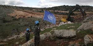 UN peacekeepers hold their flag,as they observe Israeli excavators attempt to destroy tunnels built by Hezbollah near the border in 2019.