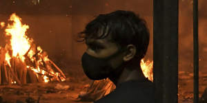 People watch burning funeral pyres of their relatives who died of COVID-19 in a ground that has been converted into a crematorium in New Delhi.