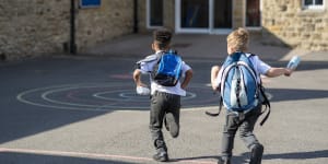 Rear view of two boys running in their school yard in the North East of England. They are running towards the door with their backpacks on. Primary school students generic image.