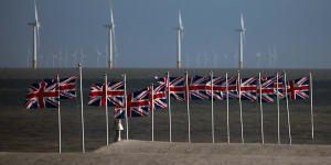 British Union flags,also known as Union Jacks,fly against a backdrop of offshore wind turbines off the coast in Clacton On Sea,England.