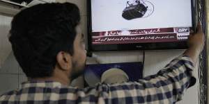 A man watches a news channel airing news regarding people trapped in a cable car,at a barber shop in Lahore.