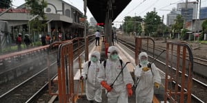 Members of the Indonesian Red Cross Society spray disinfectants on railings on a platform at the Kemayoran train station in Jakarta.