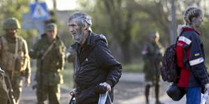 A man who left a shelter in the Metallurgical Combine Azovstal walks to a bus between servicemen of Russian Army and Donetsk People’s Republic militia in Bezimenne village in Mariupol district.