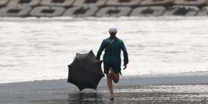 Australian medical officer Jason Patchell chases an umbrella down Tsurigasaki beach in typhoon conditions on day four of the Tokyo Olympics surfing competition.
