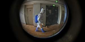 Seen through a door peephole,a medical worker wearing a protective clothing disinfects the corridor of a hotel used for foreigners to stay during a period of health quarantine in Shanghai in August. 