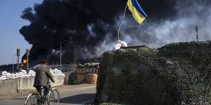 A man rides a bicycle as black smoke rises from a fuel storage of the Ukrainian army following a Russian attack,on the outskirts of Kyiv. 