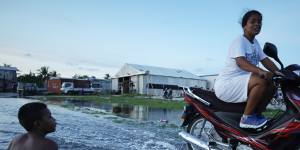 A woman rides her scooter through floodwater in Tuvalu’s capital,Funafuti,in November 2019.