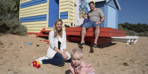 Estelle Graham,18 months,plays in the sand in front of her family’s Brighton beach box under the watchful eye of her parents Jenna and Matt and five-year-old brother Angus.