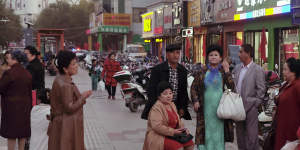 A group of older Turpan locals wait,in western dress,in front of a market.