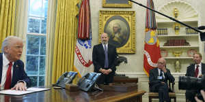 President Donald Trump signs an executive order as commerce secretary nominee Howard Lutnick (standing) and billionaires Rupert Murdoch and Larry Ellison sit in the Oval Office.