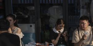 A couple sit next to a large misting fan as they wait for a table outside a popular local restaurant during a heatwave in Beijing,China,on June 23.