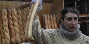 Mylene Poirier talks to a customer as she takes a baguette at a bakery,in Versailles,west of Paris.