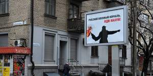 A man walks past a billboard that says “Russian military ship! Go f--- yourself” on the streets of Dnipro.