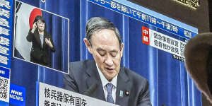 People walk through the Shinjuku area as the Prime Minister is seen on a large screen announcing the state of emergency.