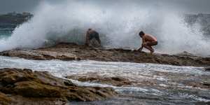 Boys hang onto the rocks as strong winds batter the coastline at Ben Buckler Point.