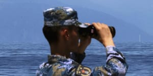 A People’s Liberation Army member watches military exercises,with Taiwan’s frigate Lan Yang in the background.