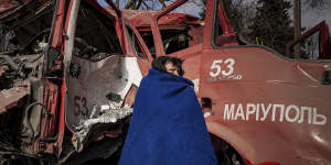 In a city that has had no heating for a week,a woman wraps herself in a blanket as she walks past the shell of a Mariupol fire truck hit by a missile. 