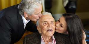 Actor Kirk Douglas,centre,gets a kiss from his son Michael Douglas,left,and Michael's wife Catherine Zeta-Jones during his 100th birthday party.