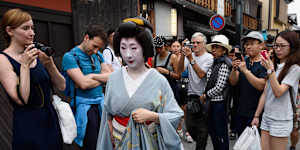 Tourists photograph a geiko walking through Gion in Kyoto.