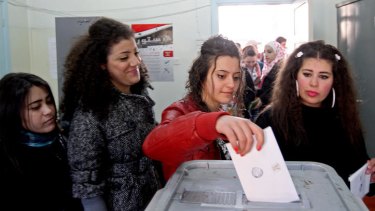 A Syrian woman casts her ballot as others queue to vote on a new constitution at a polling station in Damascus.