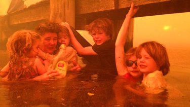 Tammy Holmes and her grandchildren, Charlotte Walker, 2, left, Esther Walker, 4, third from left, Liam Walker, 9, Matilda, 11, second from right, and   aleb Walker, 6, right, take refuge under a jetty as a wildfire rages nearby  in the Tasmanian town of Dunalley.