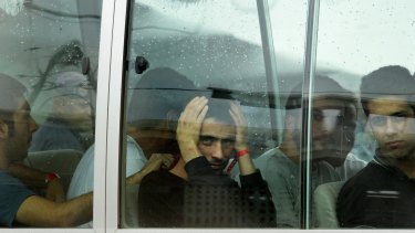 Pezhma Ghorbani (centre,hands on head), 26, from Iran looks out the window of the bus after arriving a plane carrying asylum seekers to Manus Island in 2013.