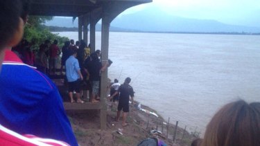 Locals watch as debris from the plane washes ashore on the banks of the Mekong River.