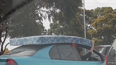 A woman holds on to a mattress on the roof of her car.