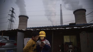 BEIJING, CHINA - NOVEMBER 27: Chinese boys look at their smartphone in front of their house next to a coal fired power plant on November 27, 2015 on the outskirts of Beijing, China.  China's government has set 2030 as a deadline for the country to reach its peak for emissions of carbon dioxide, what scientists and environmentalists cite as the primary cause of climate change. At an upcoming conference in Paris, the governments of 196 countries will meet to set targets on reducing carbon emissions in an attempt to forge a new global agreement on climate change. (Photo by Kevin Frayer/Getty Images) ***BESTPIX***