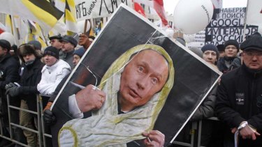 Scorned ... a protestor holds a poster showing Vladmir Putin in a white ribbon of the sort worn by protestors, which he has described as looking like condoms.