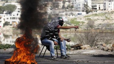 Palestinians hold stones as they sit next to a burning tyre.