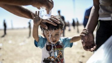 A Syrian Kurd pours water on a child after they crossed the border between Syria and Turkey near the Turkish town of Suruc.