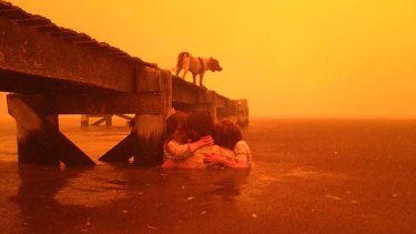 Tammy Holmes and her grandchildren take refuge under a jetty as a wildfire rages nearby in the Tasmanian town of Dunalley.