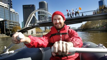 Dan Koop rows the boat and his audience joins with cast members,   seen signalling from the bridge, in a live-art journey along the Yarra during the Next Wave Festival.