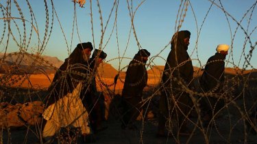A group of tribal elders walk past razor wire surrounding a police compound in Mirabad, Uruzgan province.